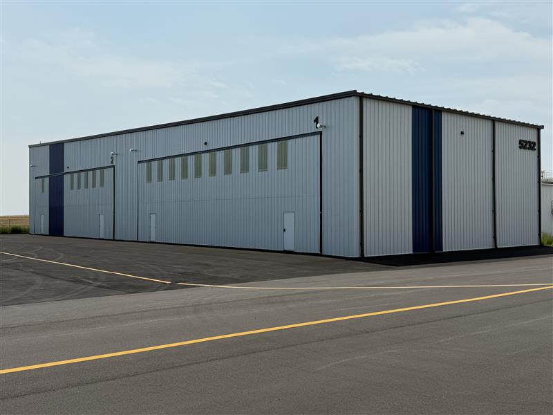 Business Aviation Group Large metal industrial warehouse with vertical blue accents, multiple doors, and windows, situated on an asphalt lot under a partly cloudy sky near Northern Colorado Regional.