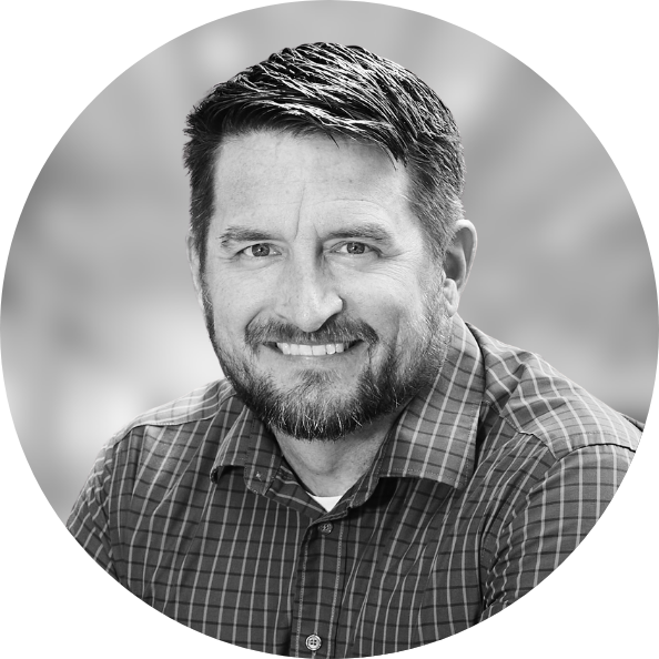 Business Aviation Group Black and white photo of a smiling man with trimmed hair and beard, wearing a checkered shirt. He's one of our valued team members, radiating confidence and camaraderie.