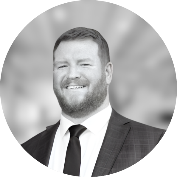 Business Aviation Group A person with a beard and short hair, dressed in a suit and tie, smiling in a black-and-white headshot with a blurred background, embodies the professionalism of our team members.