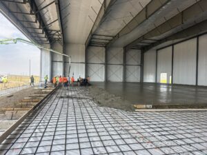 Business Aviation Group Construction workers from Tallyho Construction pour and smooth concrete over rebar inside a large, partially enclosed Hayden Executive Hangars building.