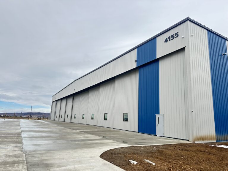 Business Aviation Group Large industrial warehouse building with blue and white exterior panels, multiple small windows, and the number 4155 above a door, seen on a cloudy day.