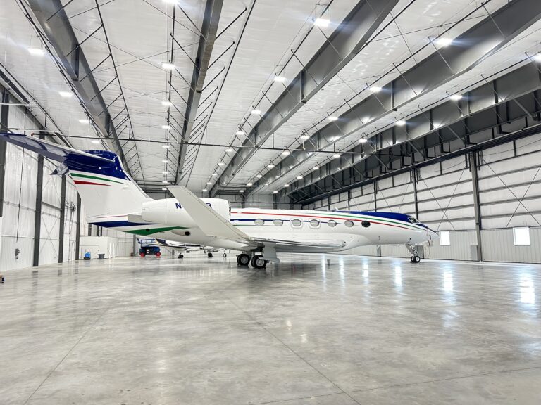 Business Aviation Group A white private jet with blue, green, and red stripes parked inside a spacious, modern airplane hangar with a concrete floor.