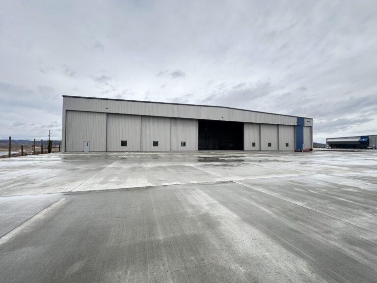 Business Aviation Group A large, gray industrial warehouse stands on a wide, empty concrete lot under an overcast sky.